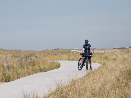 Frau mit Fahrrad auf einer Küstenstraße, bereit für eine Fahrradtour in der Nähe von Amsterdam.