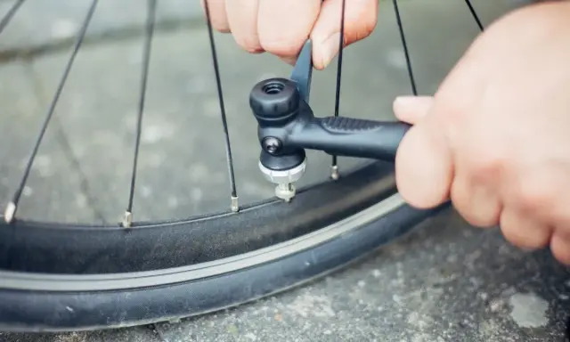Hände pumpen mit einer Handpumpe Luft in ein Fahrradventil.