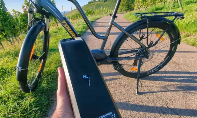E-Bike Akku wird abgenommen, um das E-Bike zu reinigen. Die Sonne scheint auf die Weinberge.