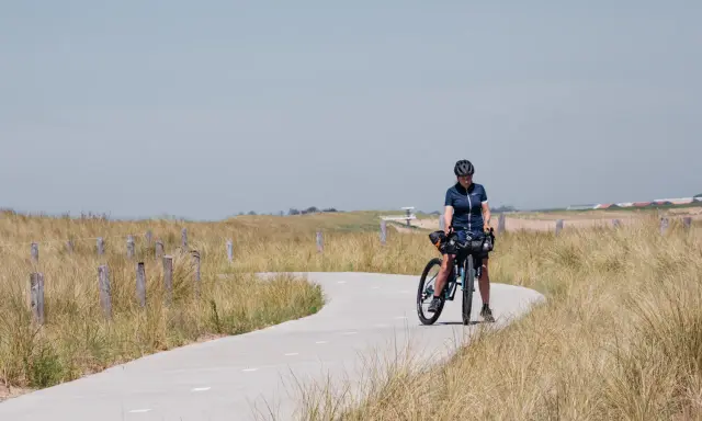 Frau mit Fahrrad auf einer Küstenstraße, bereit für eine Fahrradtour in der Nähe von Amsterdam.