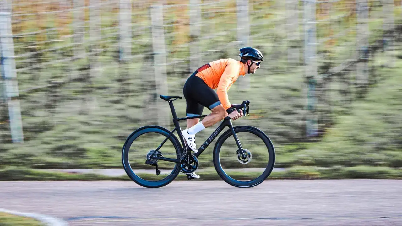 Radfahrer im orangefarbenen Trikot testet das Cube Litening Air mit aerodynamischer Haltung auf einer Straße.