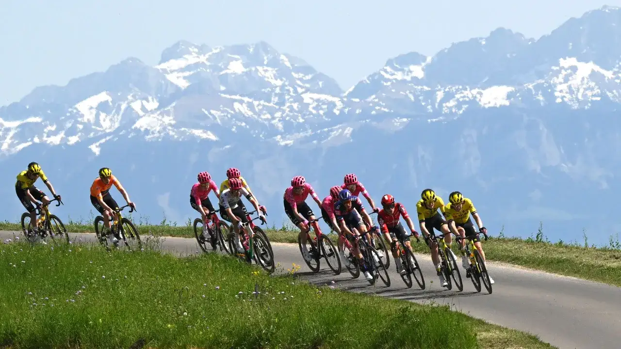 Radfahrer kämpfen sich bergauf bei der Dauphiné Rundfahrt, schneebedeckte Berge im Hintergrund.
