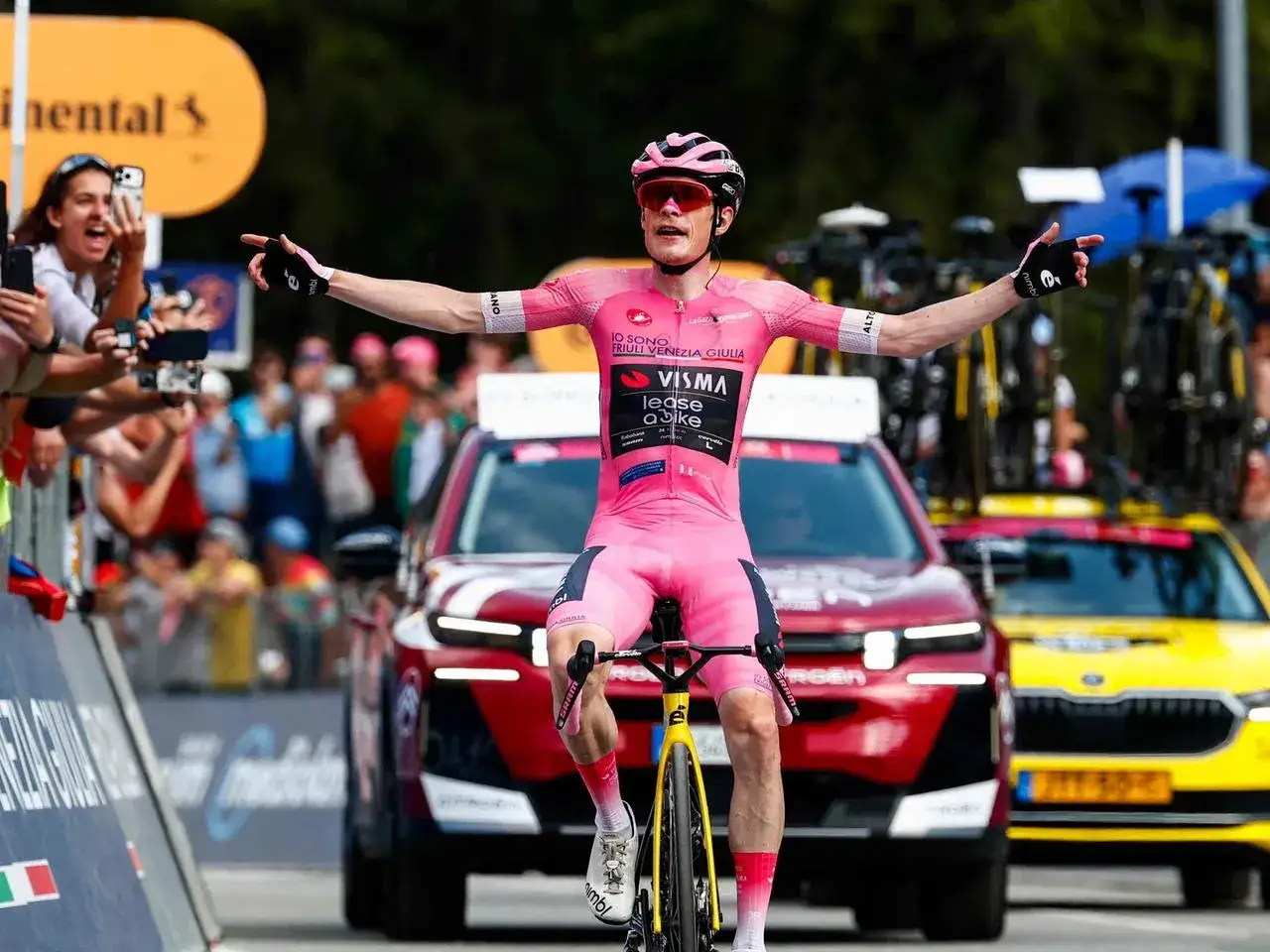 Jonas Vingegaard feiert seinen Sieg im knallpinken Trikot, die Arme triumphierend ausgestreckt. Fans jubeln ihm zu.