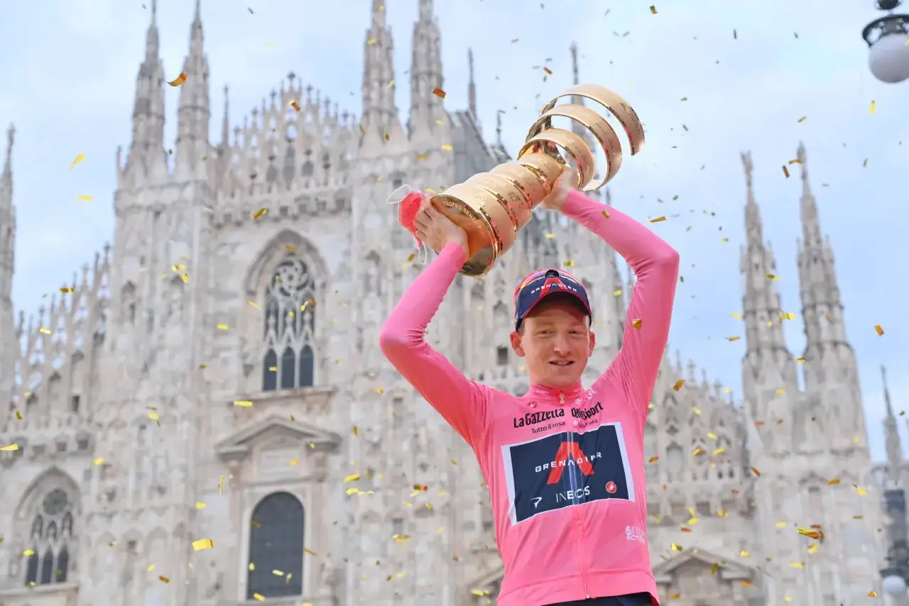 Tao Geoghegan Hart feiert seinen Sieg mit der Trophäe vor dem Mailänder Dom, während Konfetti fällt.