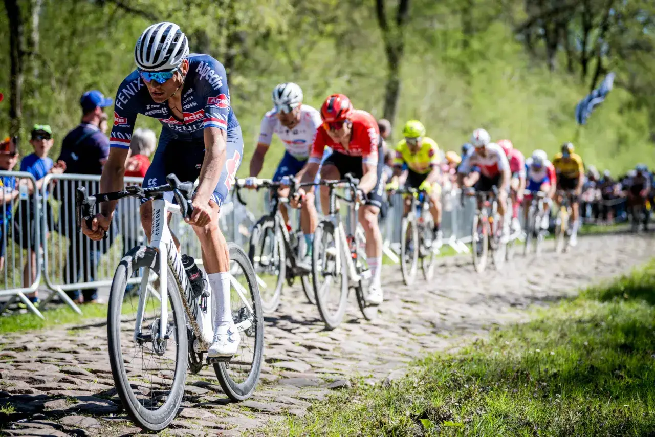 Radprofis kämpfen auf Kopfsteinpflaster um die Vorherrschaft. Ein Fahrer im Vordergrund, Teil der monumente des radsports, gibt alles.