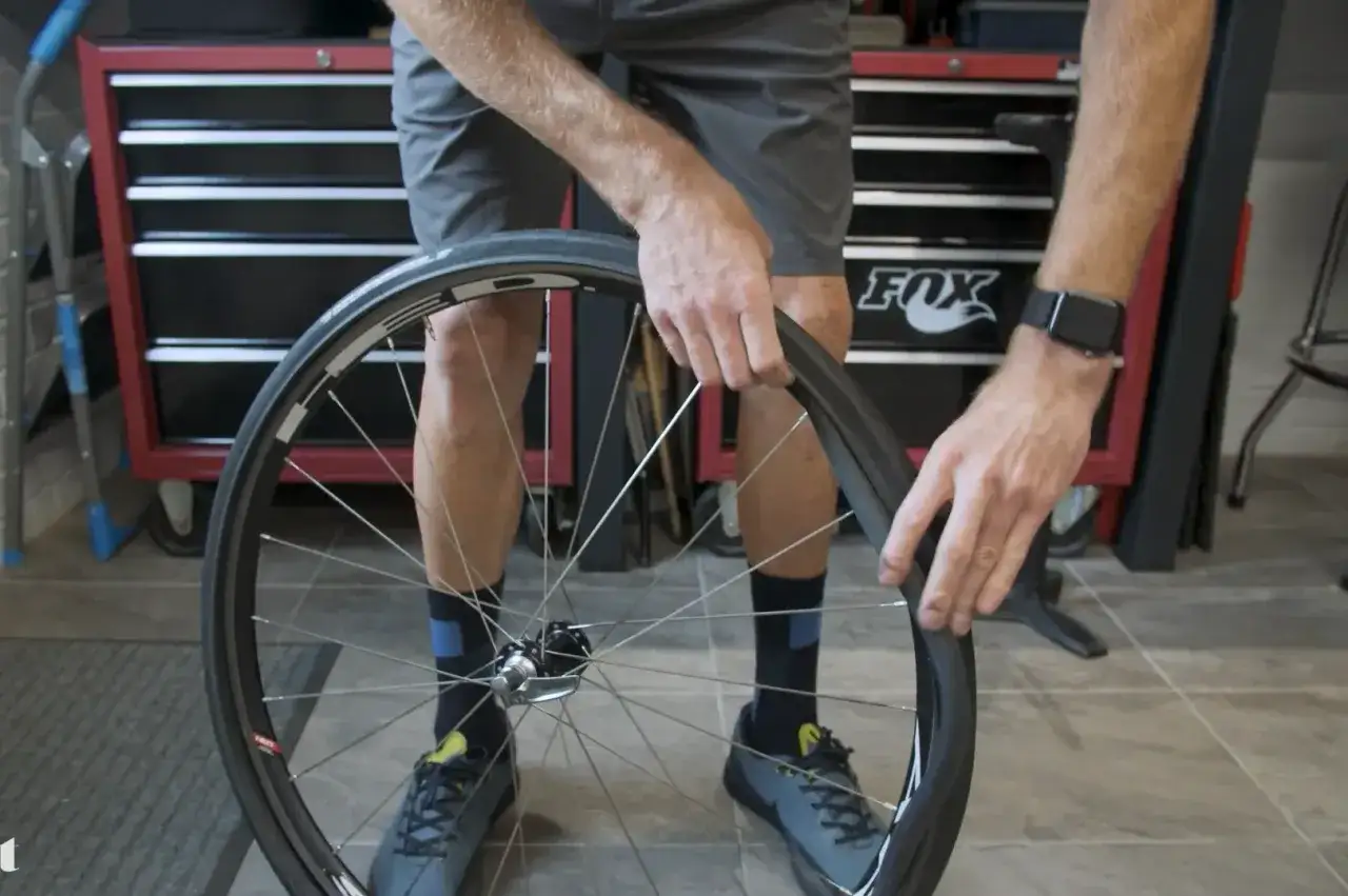 Mann wechselt den Rennrad Reifen. Er zieht den alten Reifen von der Felge ab, um ihn zu ersetzen.