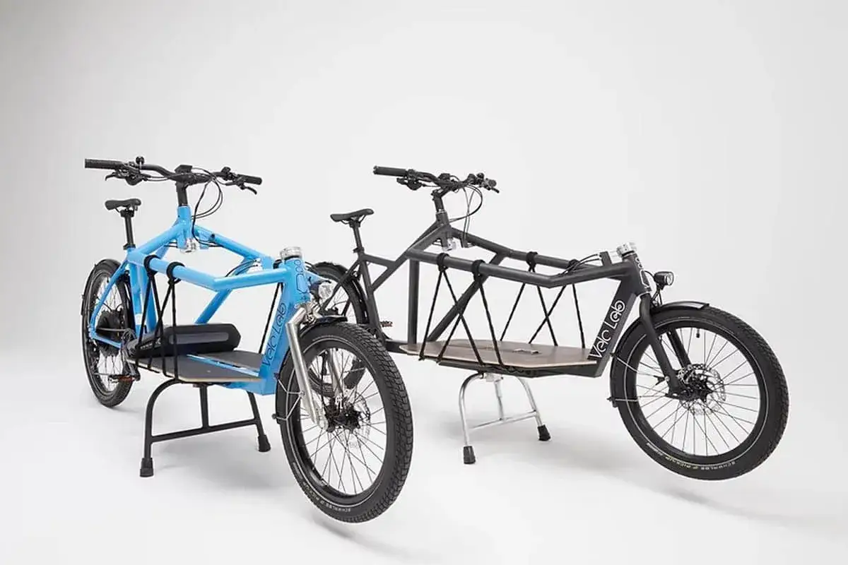 Zwei Lastenräder von Velo Lab, eins blau, eins schwarz, stehen nebeneinander.