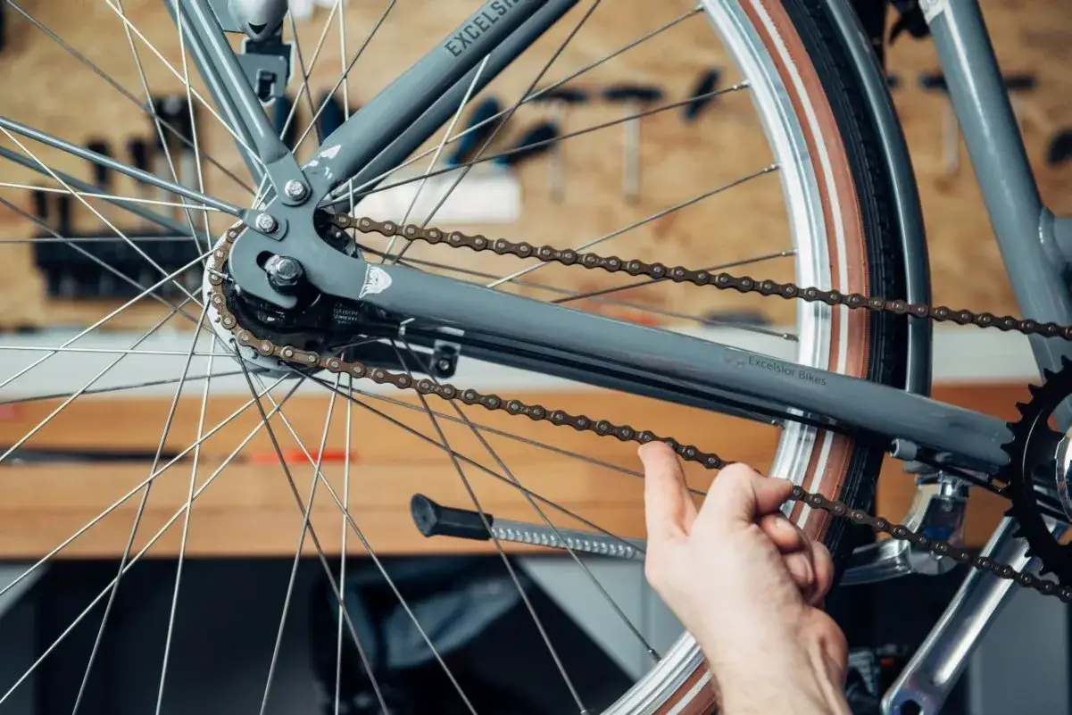 Hand prüft die Spannung der Fahrradkette an einem grauen Rad.