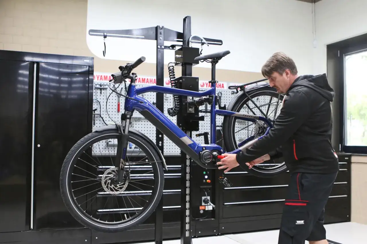 Mann führt Yamaha E-Bike Software Update durch. Das blaue Fahrrad hängt in einer Werkstatt an einem Ständer.