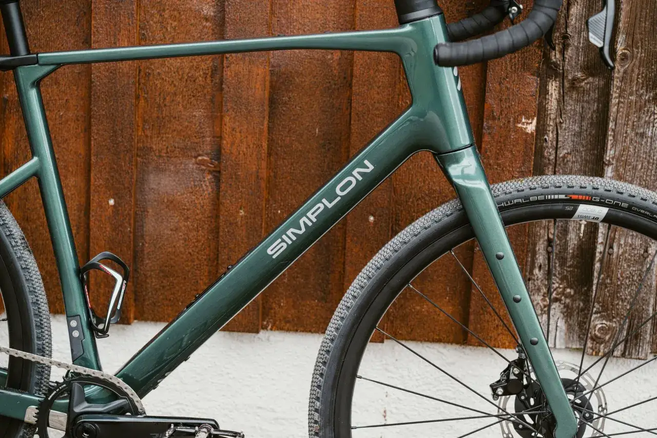 Grünes Simplon Grid Gravelbike lehnt an rustikaler Holzvertäfelung.
