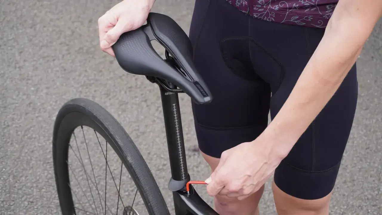Person stellt Fahrradsattel ein, die Sattelstütze hat eine Höhenmarkierung, die einer Tabelle ähnelt.
