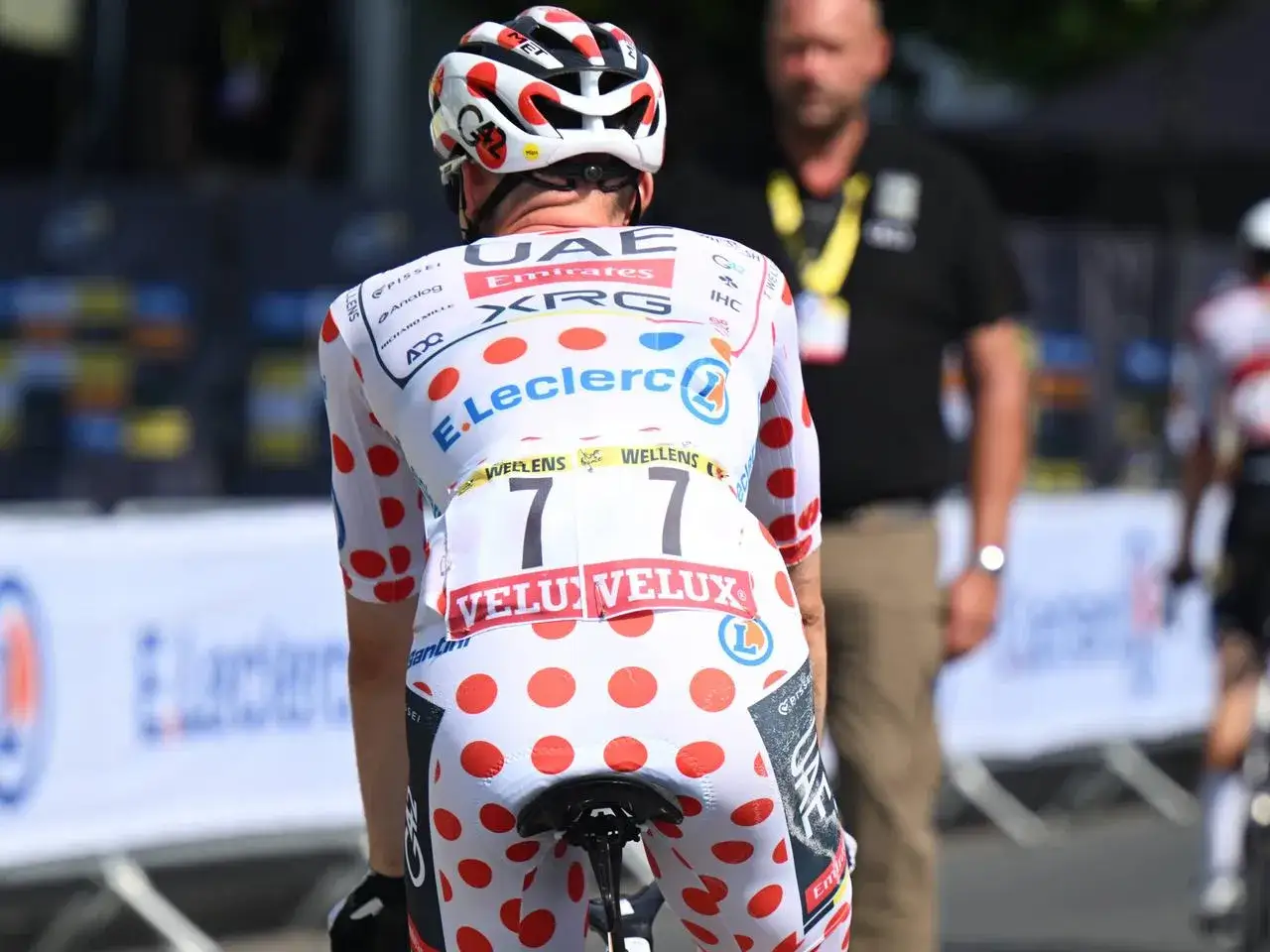 Radfahrer im ikonischen weißen Trikot mit roten Punkten, den Trikotfarben der Tour de France, bereit für die nächste Etappe.