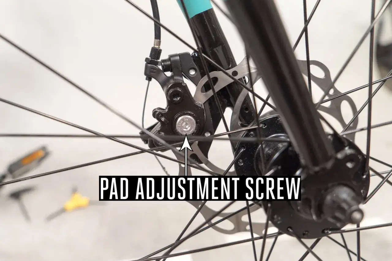 Nahaufnahme einer Fahrradscheibenbremse. Die Schraube zur Einstellung der Bremsbeläge ist markiert. Wenn diese Schraube falsch eingestellt ist, kann die Scheibenbremse schleifen.