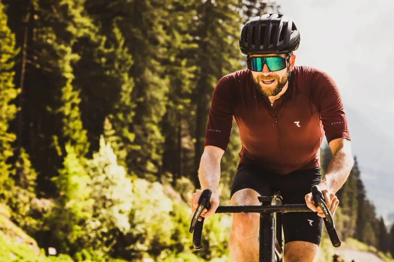 Jonas Deichmann fährt mit Helm und Sonnenbrille auf einem Rennrad durch eine sonnige Waldlandschaft.