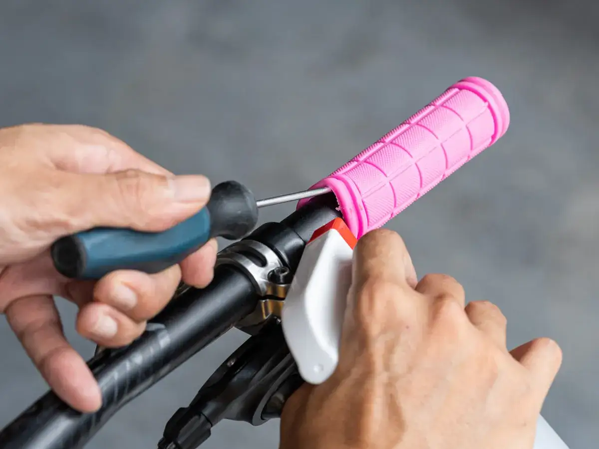 Hände wechseln pinke Fahrradgriffe mit Schraubenzieher und Sprühflasche.