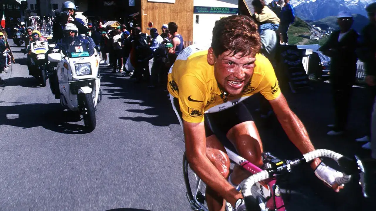 Jan Ullrich kämpft sich mit schmerzverzerrtem Gesicht und verschwitztem Körper einen Berg hinauf. Ein dramatischer Moment, der an seinen späteren Absturz erinnert.