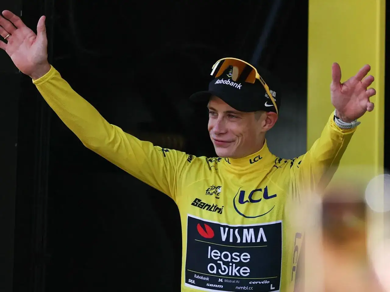 Radfahrer im gelben Trikot der Tour de France jubelt mit erhobenen Armen. Er trägt eine schwarze Kappe und Sonnenbrille.