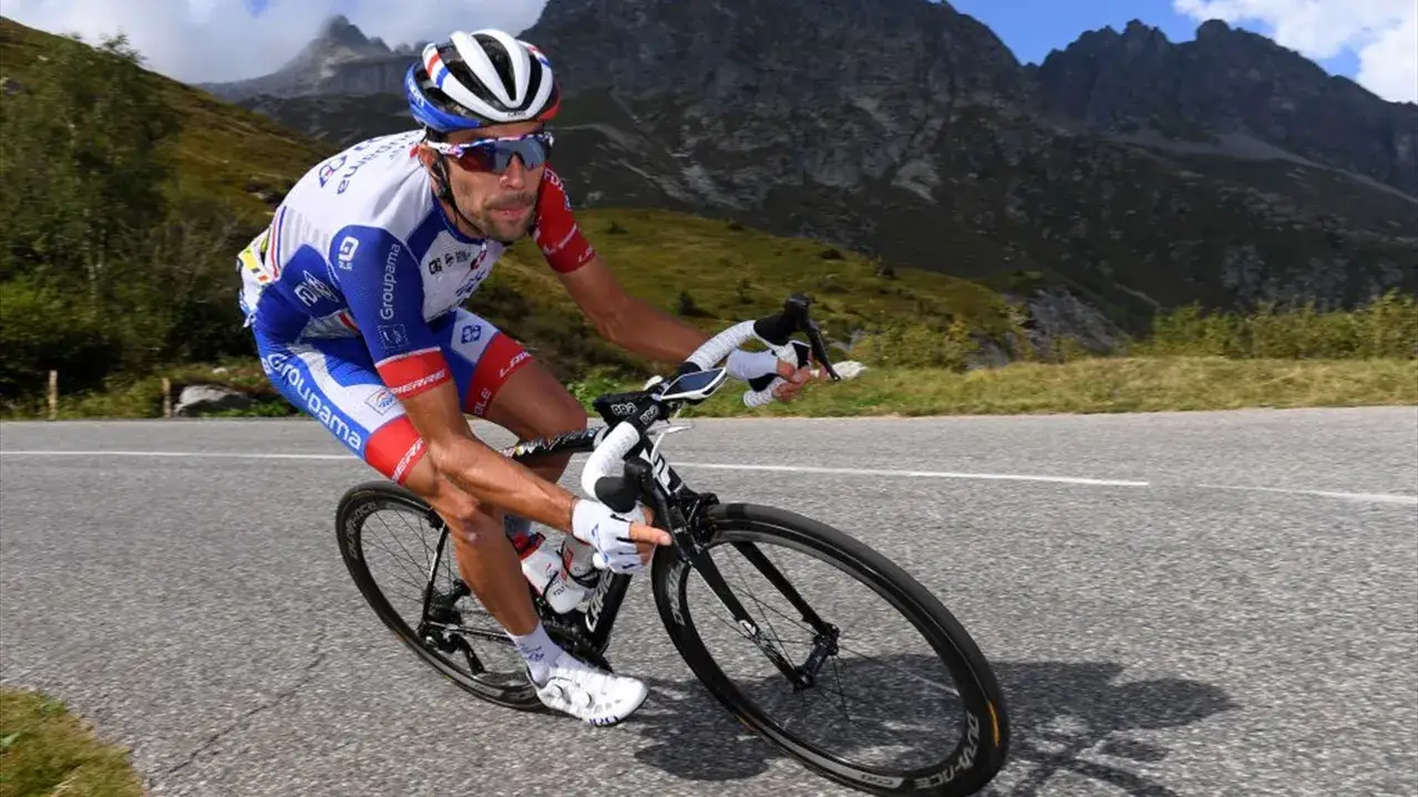 Thibaut Pinot kämpft sich auf seinem Rennrad einen Bergpass hinauf, die majestätischen Alpen im Hintergrund.