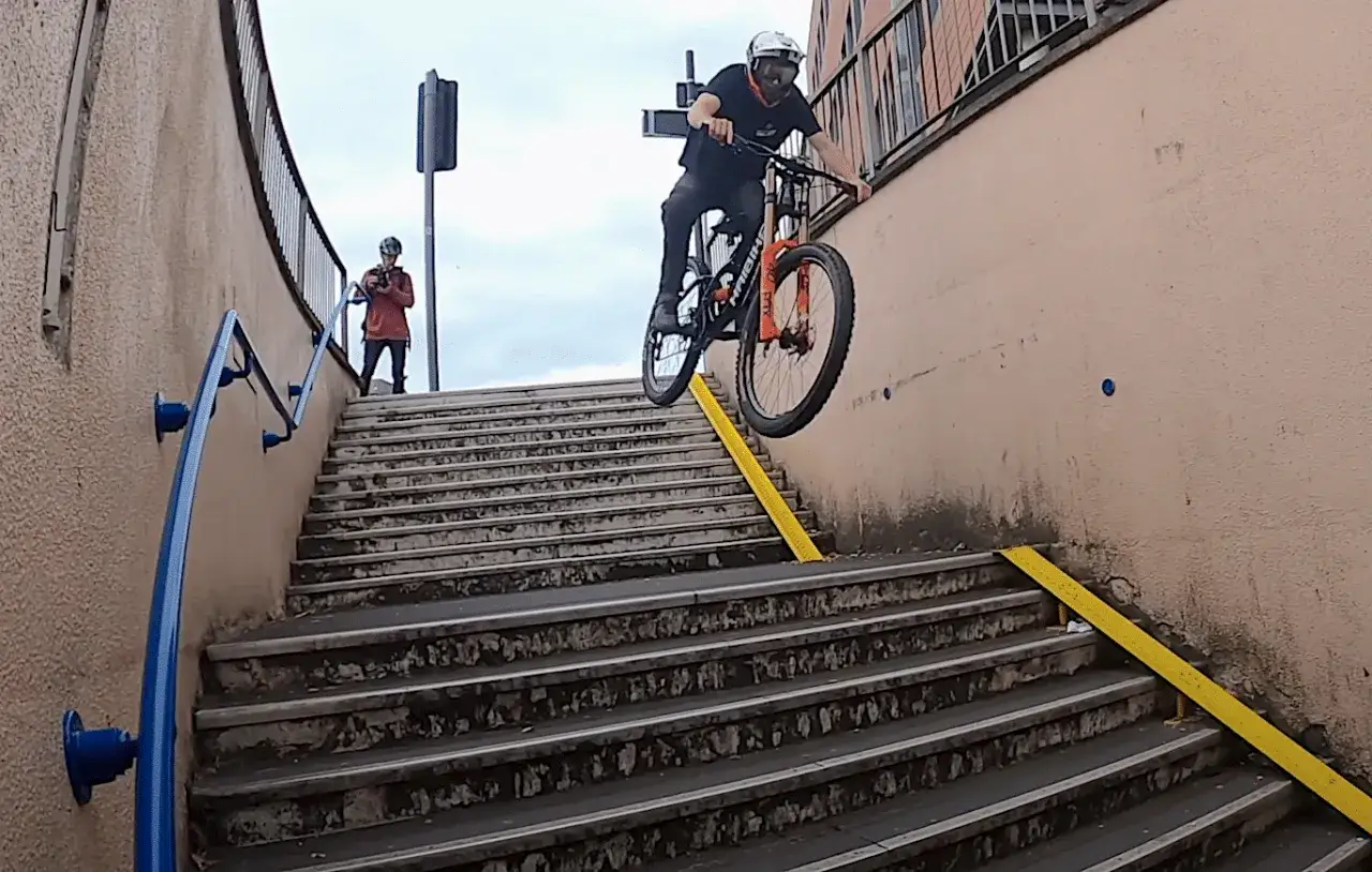 Sam Pilgrim fliegt mit seinem Mountainbike eine Treppe hinunter. Ein Freund filmt ihn.
