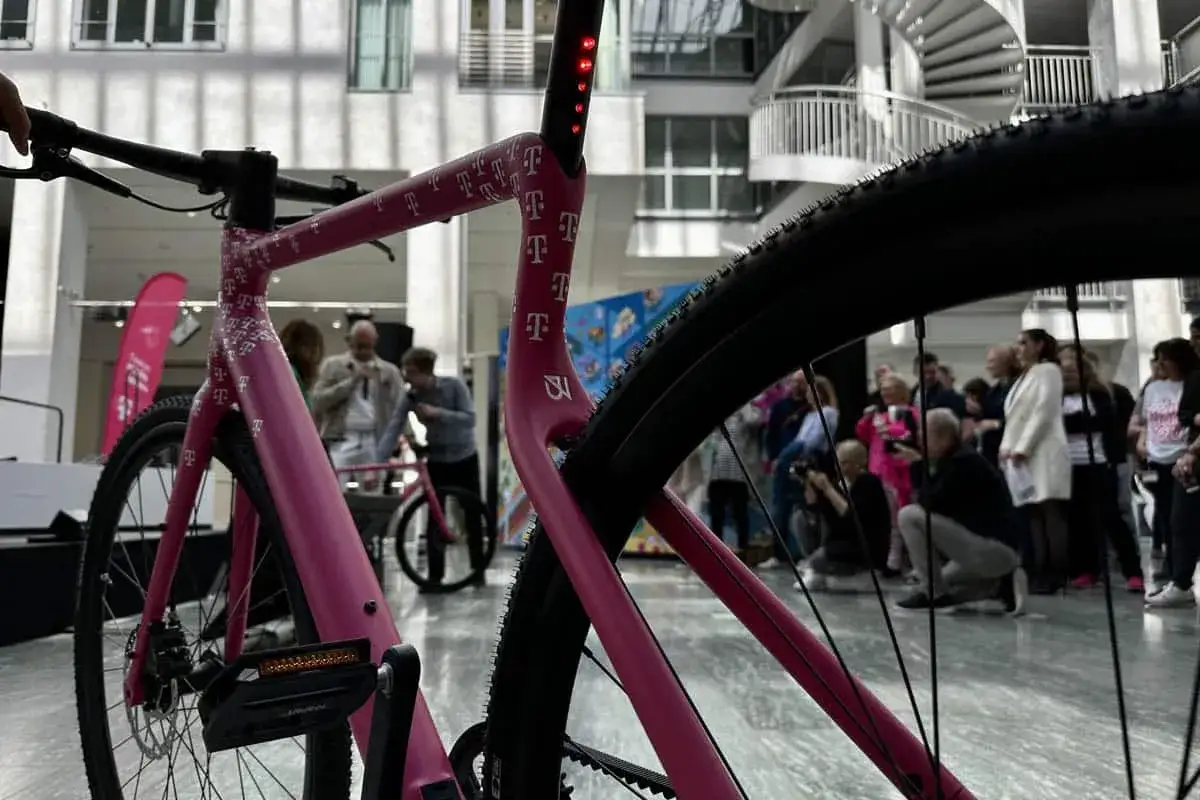 Ein pinkes company bike der Telekom mit vielen T-Logos, das auf einer Veranstaltung präsentiert wird.