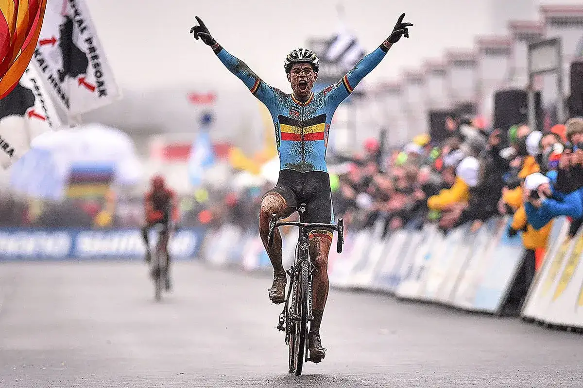 Wout van Aert feiert seinen Sieg im Schlamm-Cyclocross. Jubelnde Menge im Hintergrund.