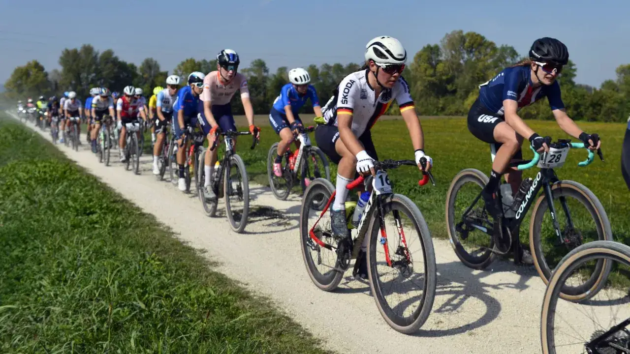 Radfahrerinnen kämpfen auf Schotter um die Gravel WM Ergebnisse. Die deutsche Fahrerin mit Startnummer 16 führt das Feld an.