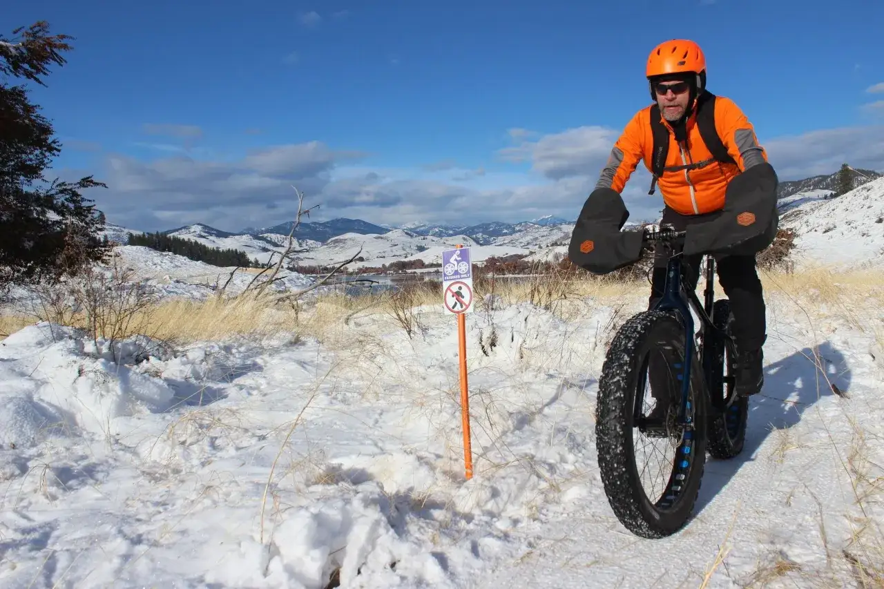 Mann fährt mit einem Fatbike durch verschneite Landschaft. Das Schild sagt