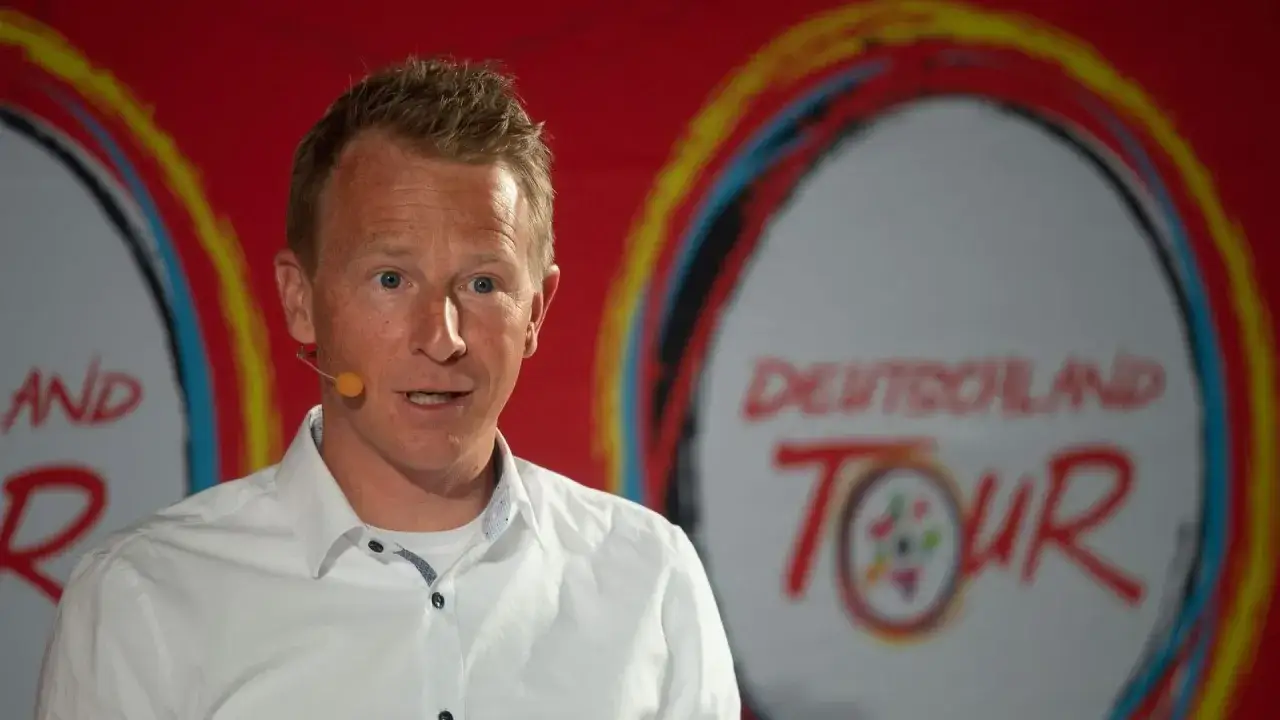 Fabian Wegmann spricht vor dem Logo der Deutschland Tour. Seine Vergangenheit mit Doping-Vorwürfen ist ein Thema.