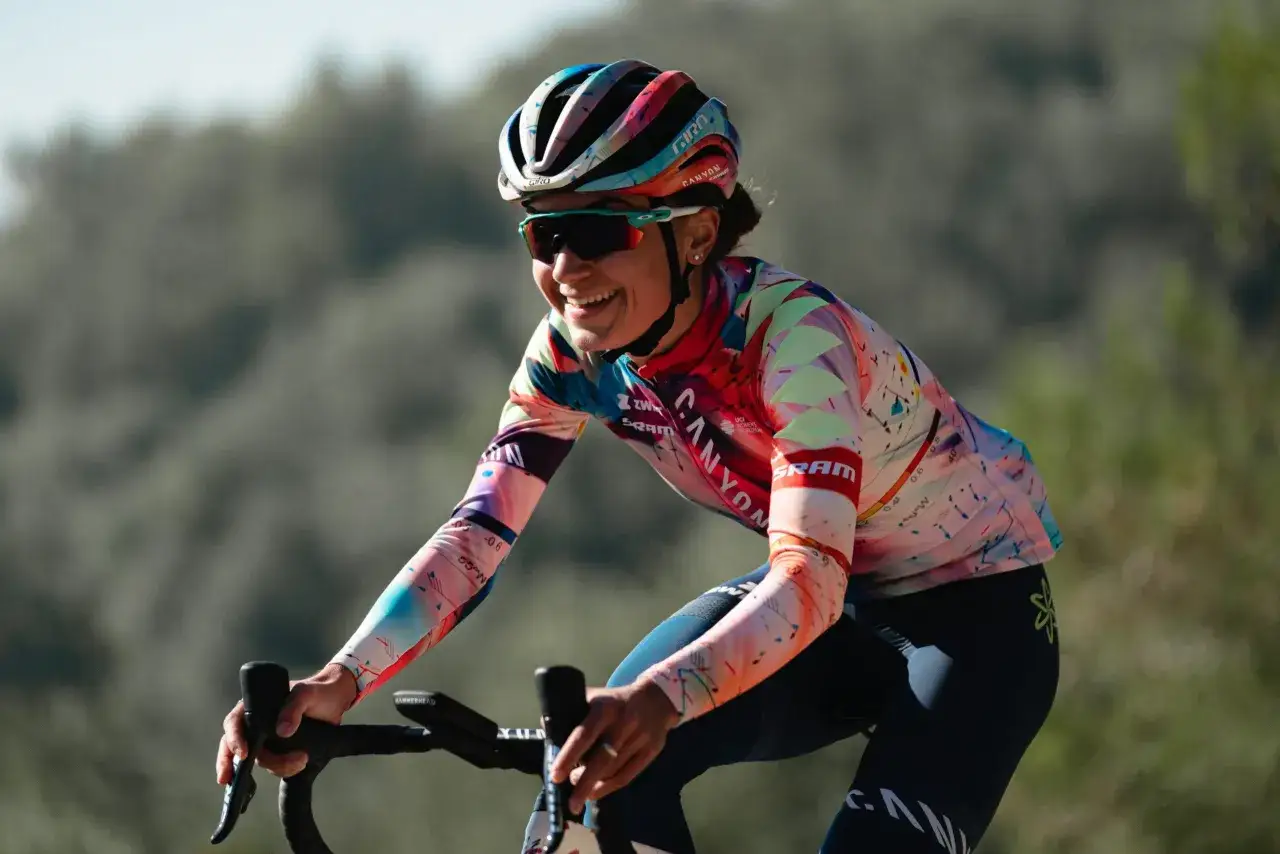 Ricarda Bauernfeind strahlt auf ihrem Rennrad, trägt einen bunten Helm und ein auffälliges Trikot.