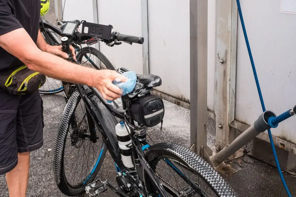 Mann reinigt sein e-bike mit einem Schwamm. Seifenschaum bedeckt das Fahrrad, während er es sorgfältig säubert.