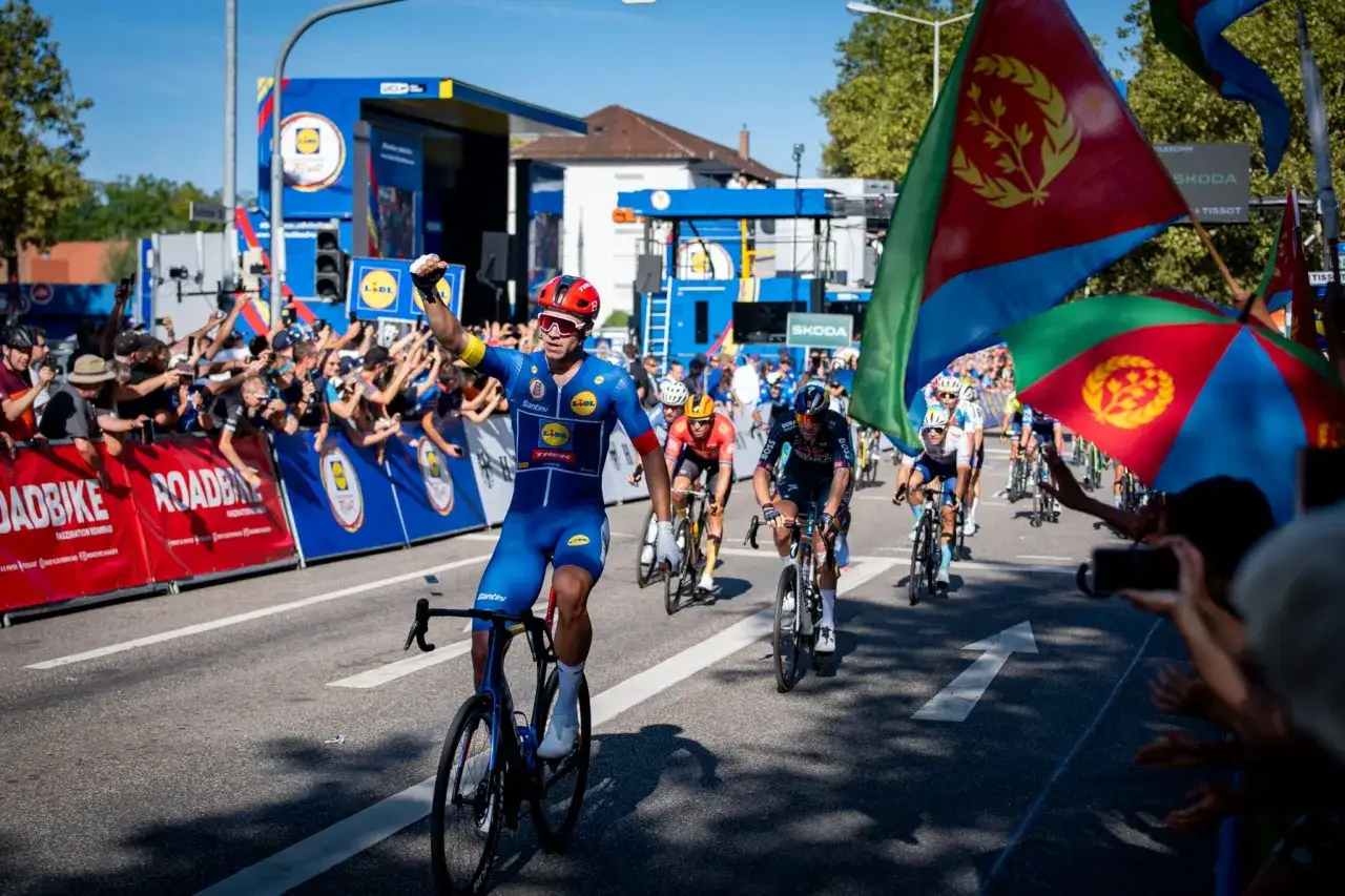 Jonathan Milan jubelt auf dem Rad, umgeben von jubelnden Fans und Flaggen.