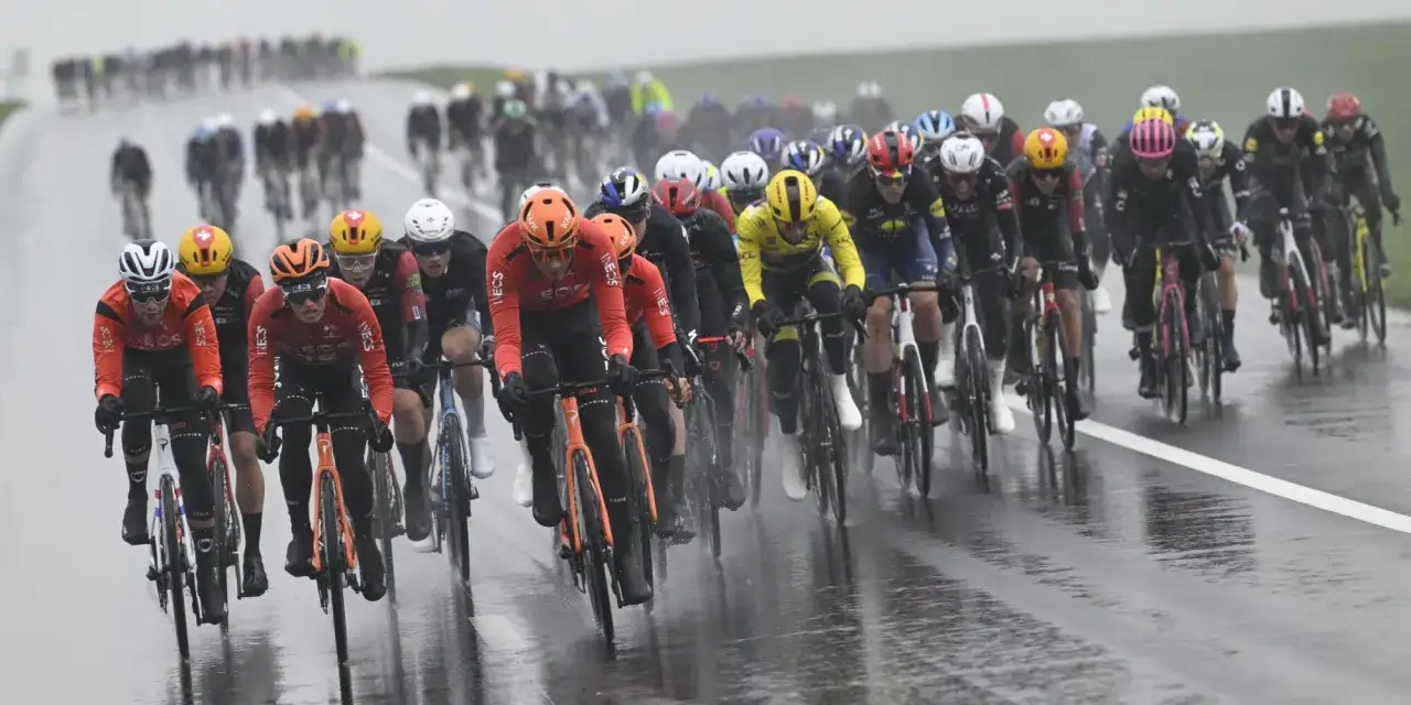 Radsport Paris-Nizza: Peloton kämpft sich durch Regen und Pfützen. Rennfahrer in roten und gelben Trikots auf nasser Straße.