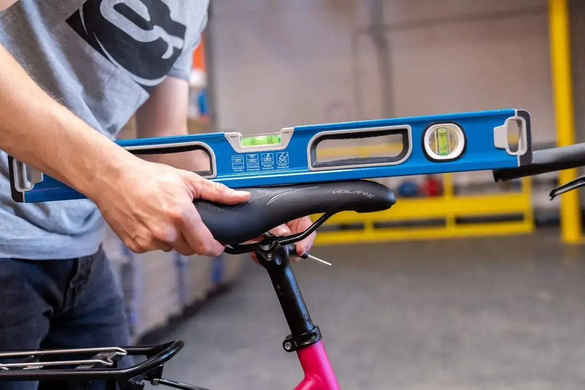 Person stellt mit Wasserwaage die sattelneigung einstellen zwei schrauben am Fahrradsattel ein.