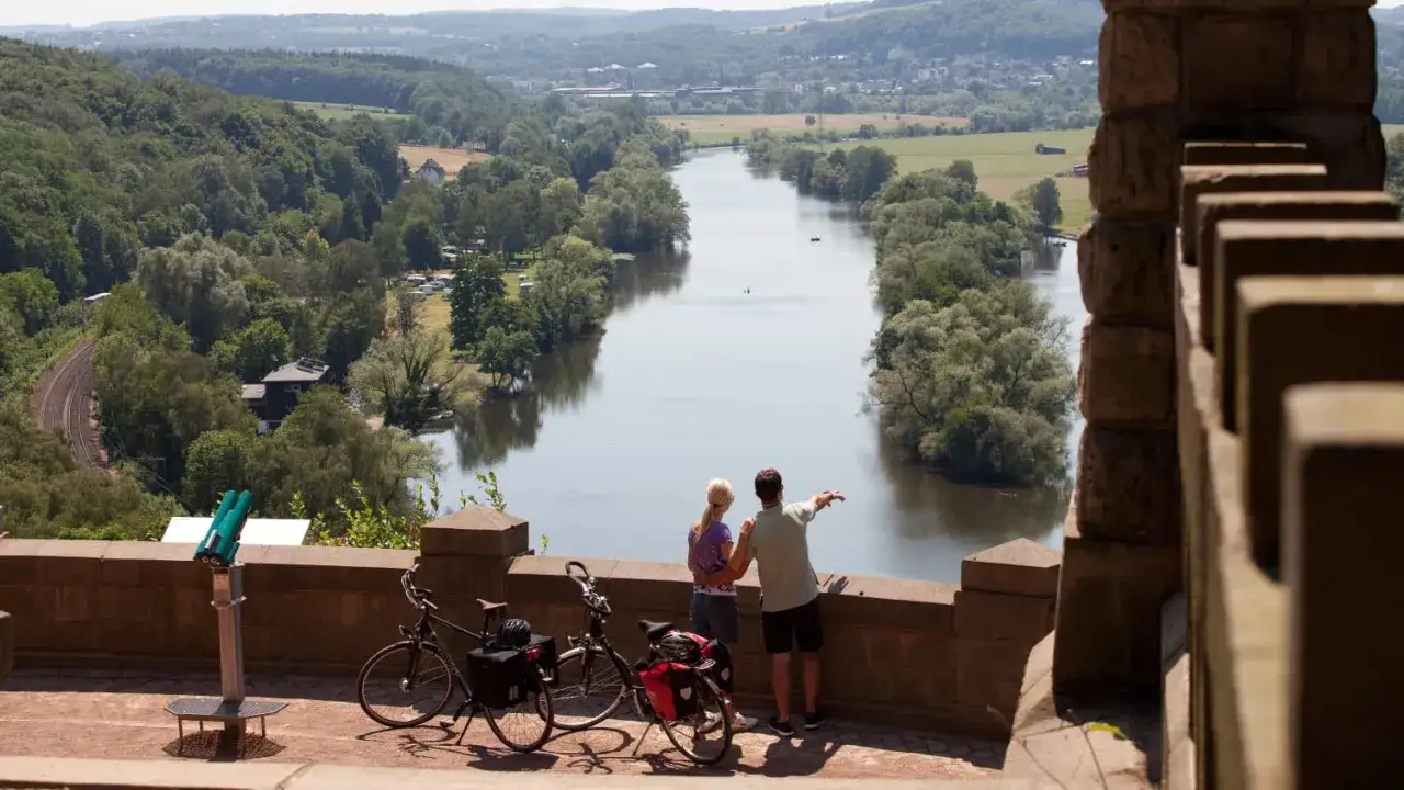Ein Paar genießt den Ausblick auf einen Fluss während einer Fahrradtour in NRW. Zwei Fahrräder stehen bereit.