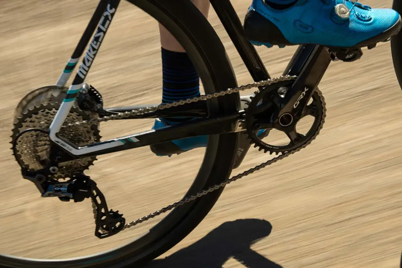 Detailaufnahme eines Fahrrads mit Shimano GRX 400 Kurbelgarnitur und Schaltwerk. Der Schuh des Fahrers ist blau.