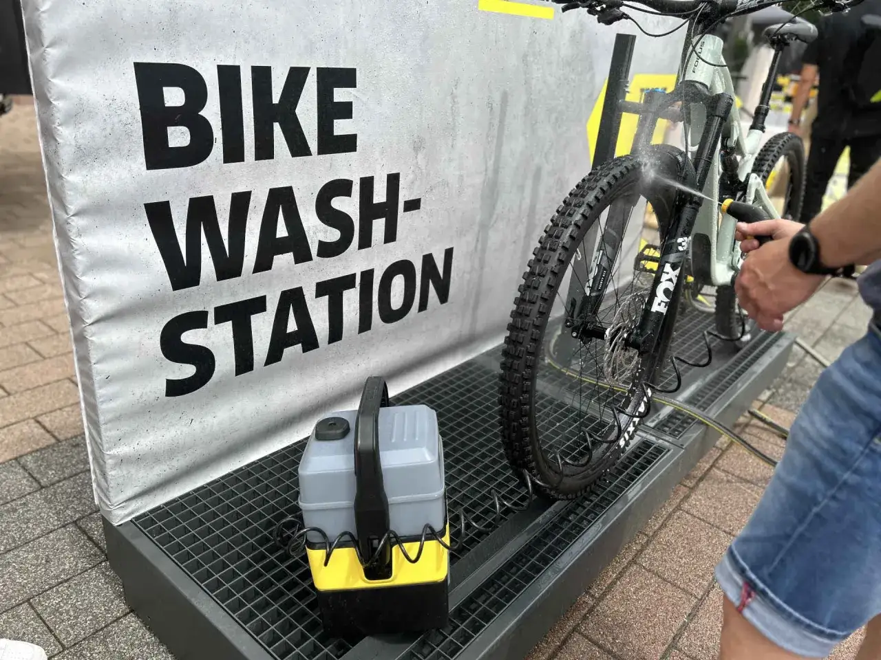 MTB reinigen an der Bike Wash Station. Ein Mann spritzt mit einem Hochdruckreiniger das Mountainbike ab.