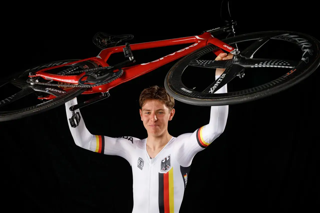 Tim Torn Teutenberg präsentiert stolz sein rotes Rennrad, ein Symbol für seine Leidenschaft und Erfolge im Radsport.