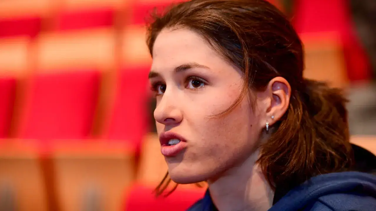 Marie Schreiber spricht, ihr Blick ist nach links gerichtet. Im Hintergrund sind rote Stuhlreihen zu sehen.