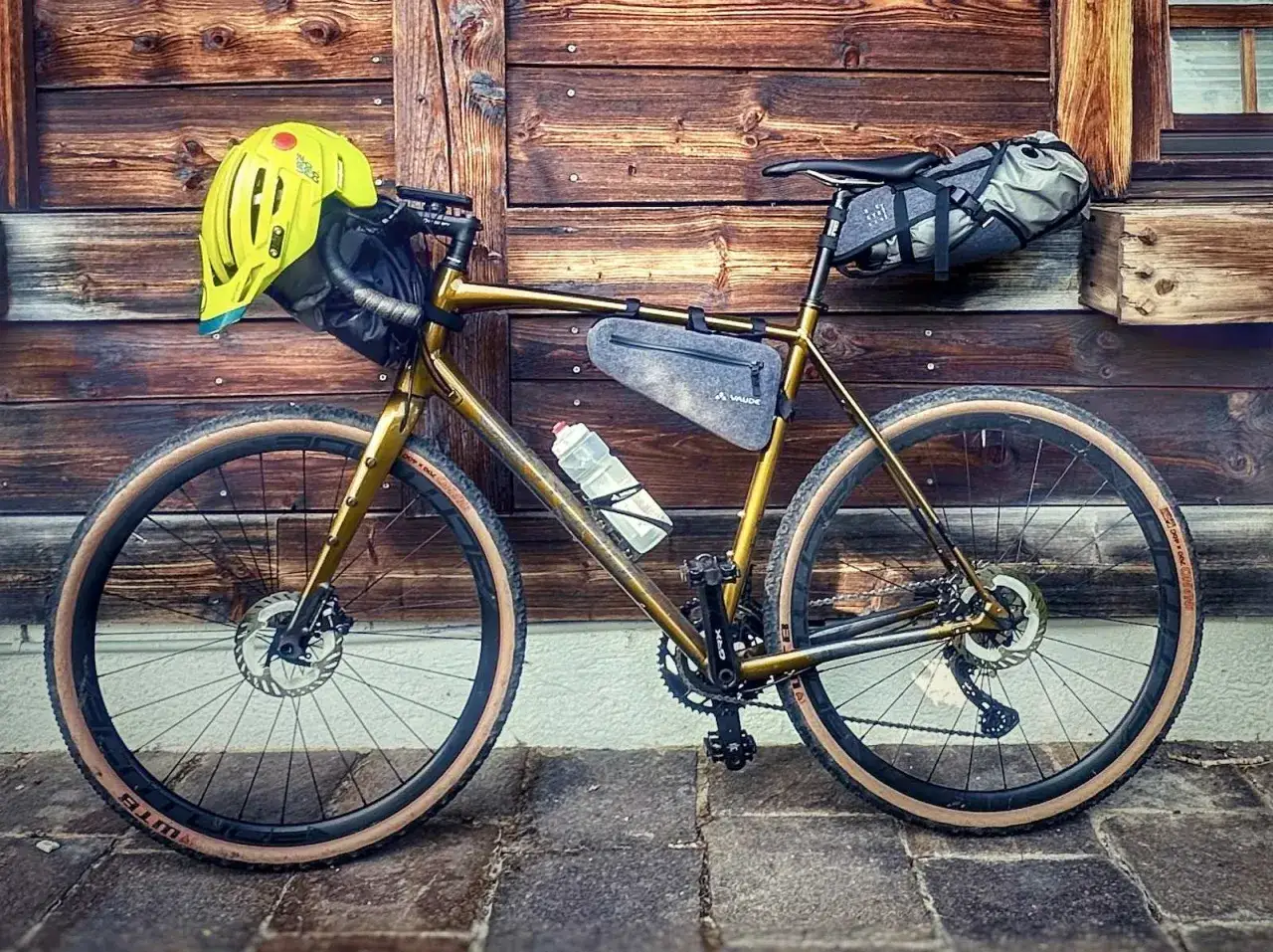 Goldenes Gravelbike mit Helm, Satteltasche und Rahmentasche, bereit für Gravel Touren Deutschland.