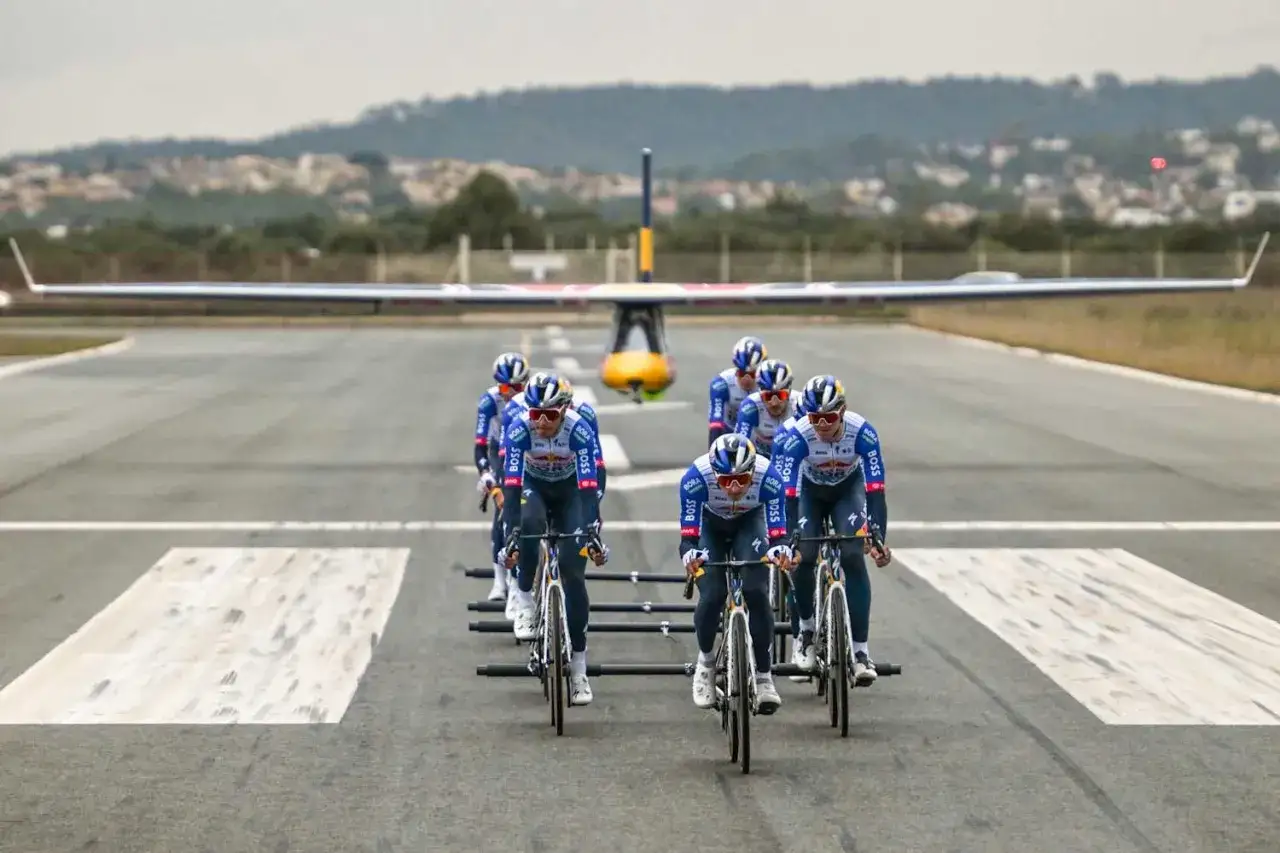 Ein Team von radrennfahrer deutsch fährt auf einer Landebahn, ein Flugzeug im Hintergrund.