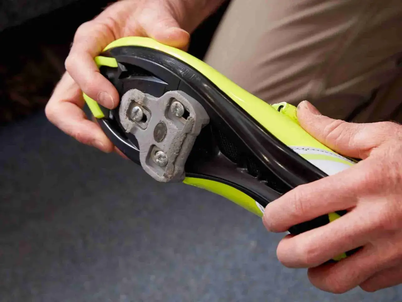 Hände stellen die Klickpedale an einem leuchtend gelben Fahrradschuh ein.