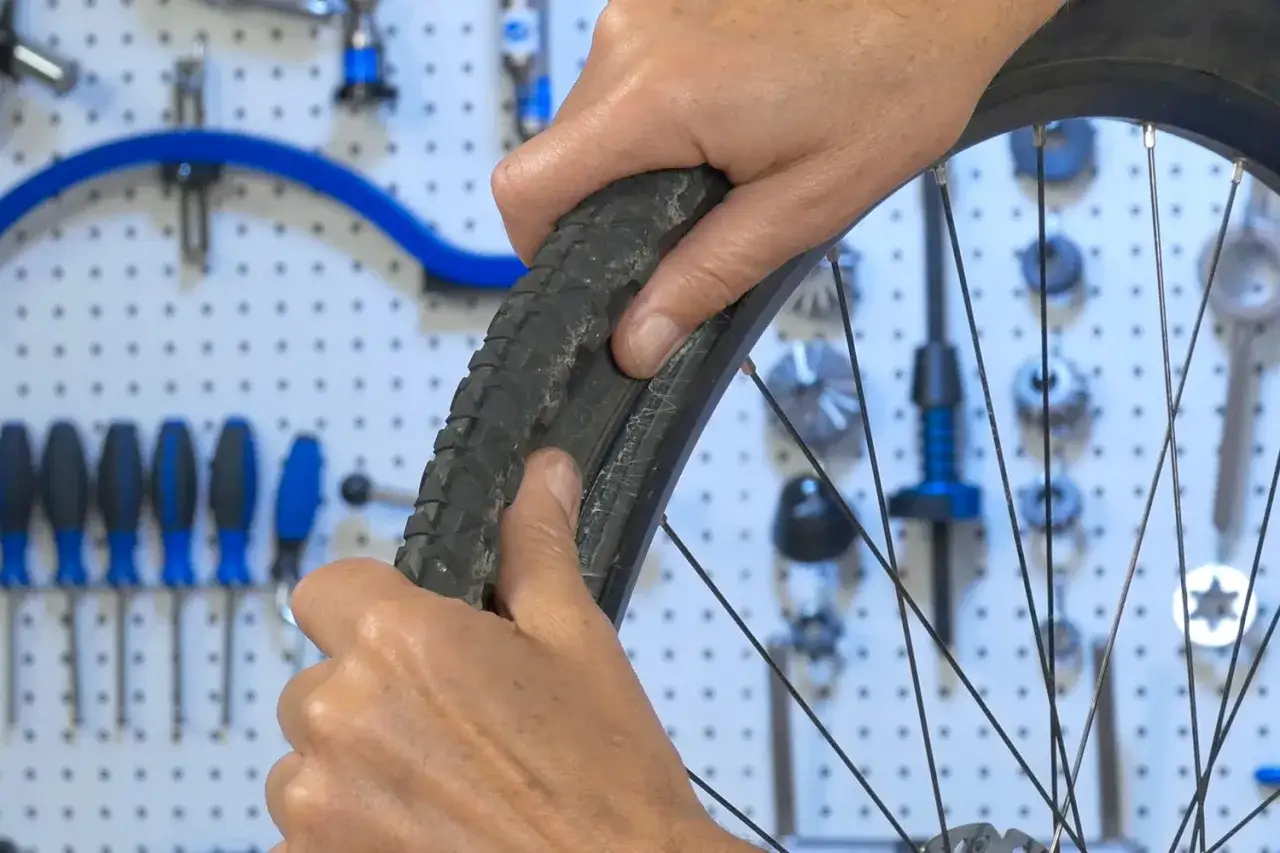 Hände montieren einen tubeless reifen. Werkzeuge hängen an der Wand im Hintergrund.