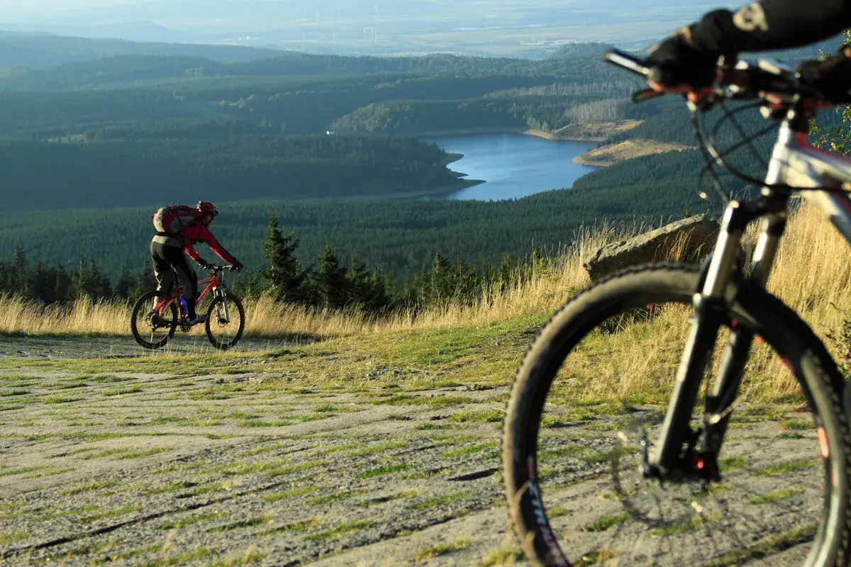 Zwei Radfahrer genie&szlig;en eine atemberaubende Aussicht bei ihren MTB Touren. Ein See und W&auml;lder erstrecken sich in der Ferne.