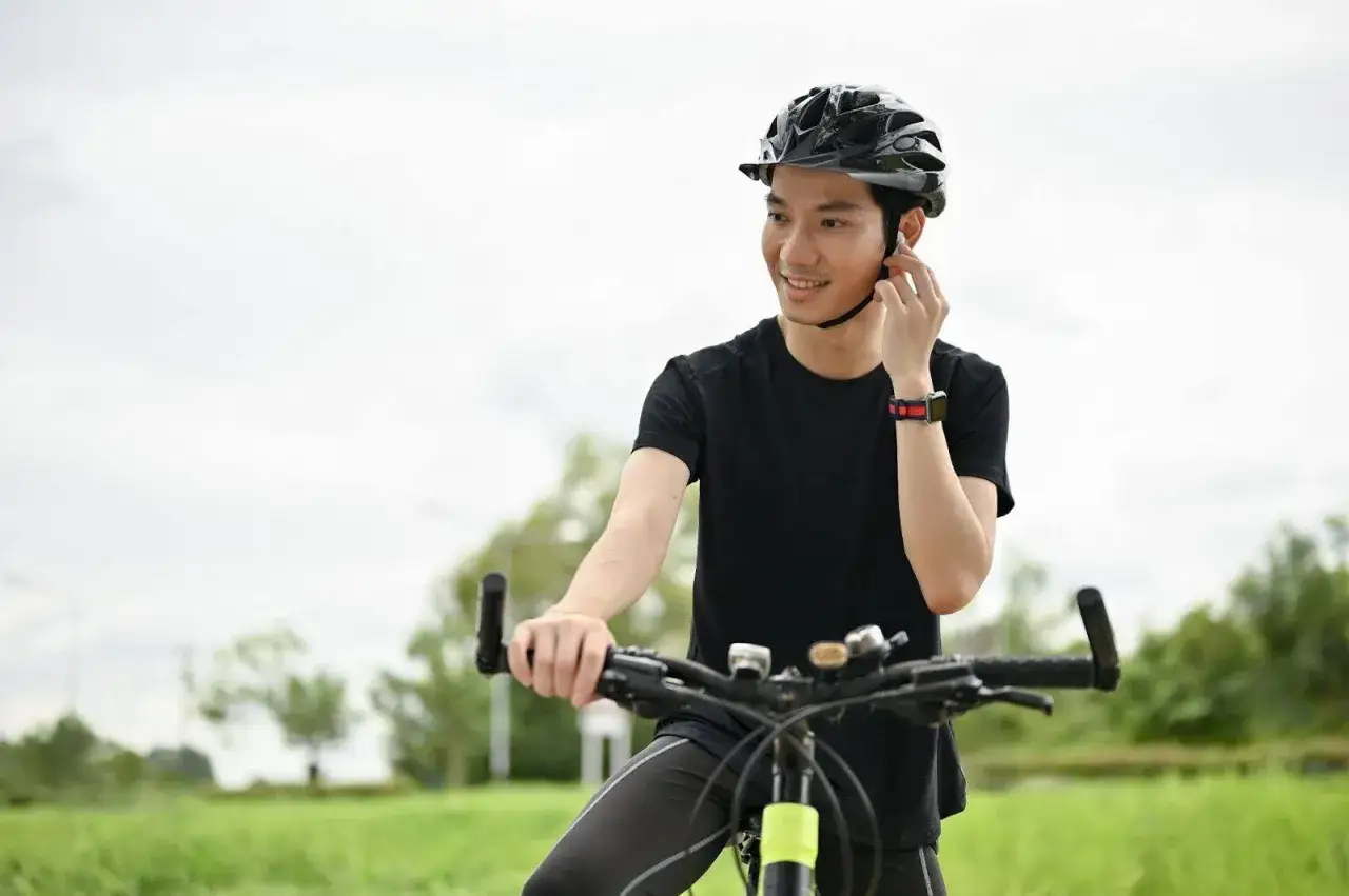 Ein Mann mit Helm auf einem Rennrad, der sich auf eine Fahrt vorbereitet und dabei Kopfhörer einstellt, vielleicht für einen Rennrad Podcast.