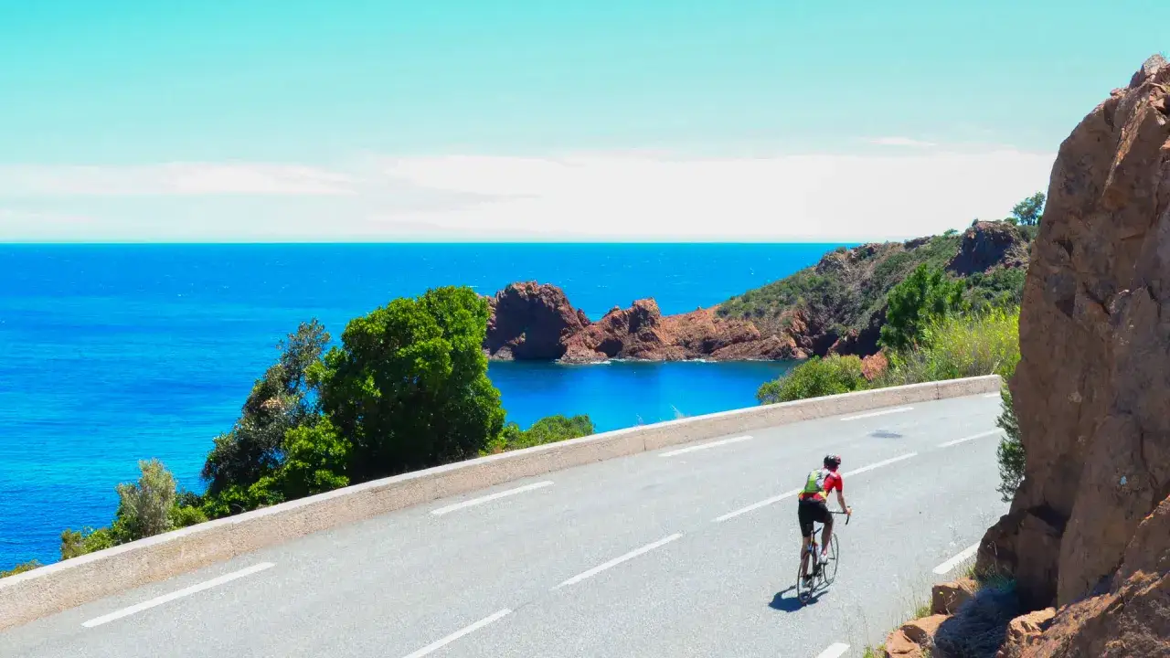 Radfahrer auf der Nizza Route genießt die atemberaubende Küstenlandschaft mit türkisfarbenem Meer und roten Felsen.