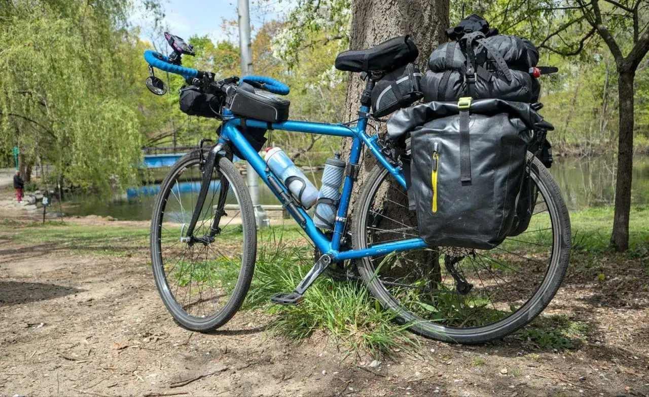 Blaues Fahrrad mit viel Gepäck, bereit für Bikepacking mit Rucksack. Wasserflaschen und Satteltaschen sind angebracht.