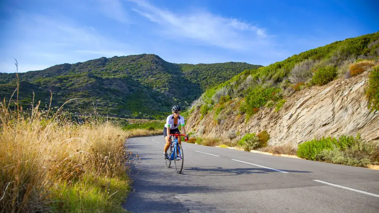 Rennradfahrerin auf Korsika genießt die bergige Landschaft unter blauem Himmel.